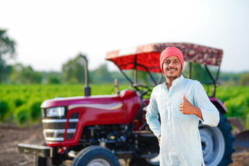 young indian farmer standing with tractor at field