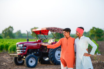 two young indian farmer standing together with tractor at field
