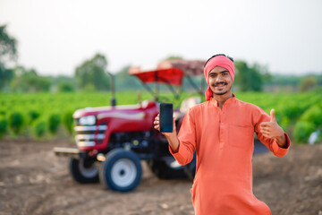 indian farmer standing with tractor and talking on smartphone at field