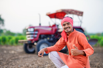 young indian farmer sitting with tractor at field