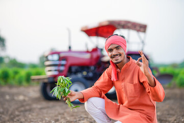 young indian farmer holding plant sitting at field