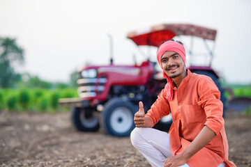 young indian farmer sitting with tractor at field