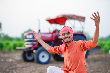 young indian farmer sitting with tractor at field