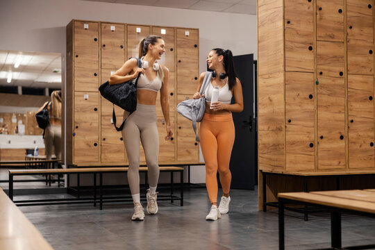 Two fit sportswomen walking into fitting room at gym and smiling at each other. - Powered by Adobe