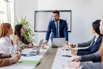 Leader is standing at conference table and having serious talk with his employees.