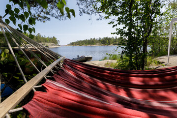 Restful view from a red hammock looking out at a calm lake, inflatable boat, and forested shoreline...