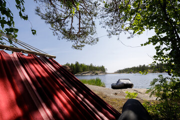 Relaxing in a striped red hammock under tree shade, looking out over a calm lake and inflatable boat at the shore.