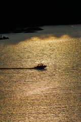 Silhouette of a motorboat gliding across a lake during sunset, reflecting golden light on the...