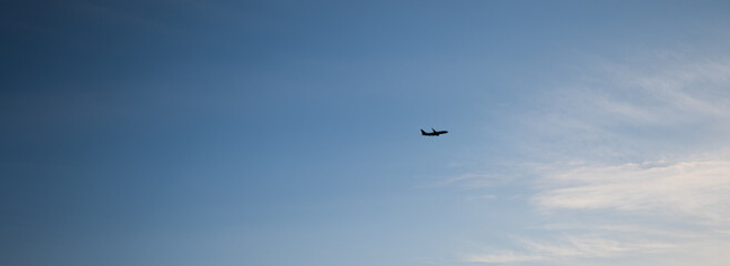 Banner image with silhouette of an airplane flying across a wide clear blue sky. Concept of air travel, airline industry, and global tourism. Ideal for travel ads, websites, or promotional use
