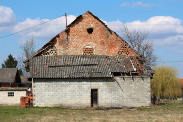 Old barn constructed of red brick and gray concrete blocks, featuring a partially collapsed tile...