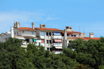 Cluster of white apartment buildings with red tile roofs and balconies rises above dense green...