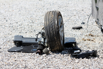 Car wheel with attached suspension and broken parts lies detached on a rough gravel surface,...