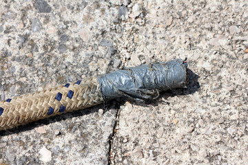 Close-up of a thick braided rope with blue accents, its end wrapped in worn grey duct tape, lying...