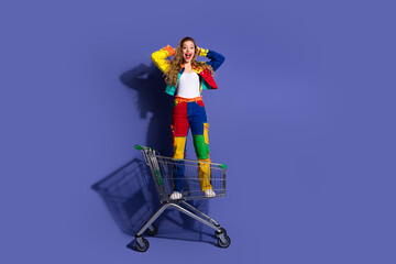 Cheerful young woman in colorful outfit posing with vibrant expression in a shopping cart on a...