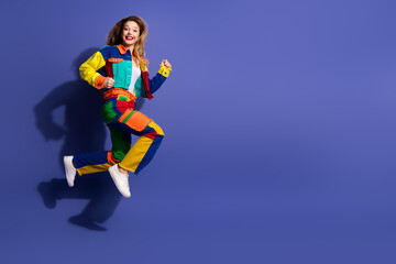 Energetic woman jumping in colorful outfit against a purple background showcasing fashion and fun