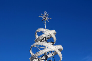 Metal-framed Christmas tree sculpture wrapped in white garland spirals, topped with a star, stands...