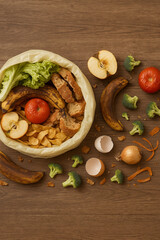Assorted wasted food and rotting produce scattered near open garbage bag on wooden table