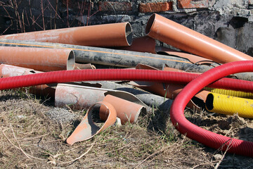 Mixed pile of orange, black, red, and yellow plastic and metal pipes, some corrugated, lies on dry...