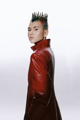 Woman with colorful hair and spiked crown wearing a red leather coat, posing confidently against a...