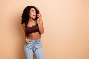 Young woman posing casually holding an apple, highlighting beauty, health, and style on a neutral...