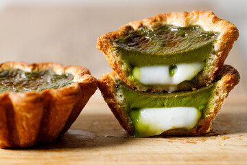 Closeup of Matcha and mochi Portuguese sweet dessert egg tart or Pastel de Nata on wooden board on...