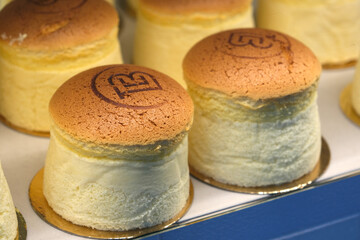 Close-up of fluffy Japanese cheesecakes with golden tops, displayed in a bakery showcase, ready for...