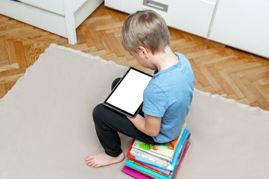 Little boy kid child sitting on stack of children's books and looking at tablet,laptop,learning read with gadget,watching cartoons.Modern technology education