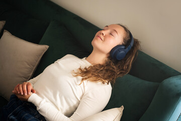 Top view young calm woman listening music in wireless headphones, closed eyes, sitting on sofa at...