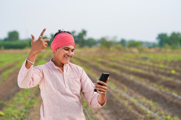 young indian farmer holding smartphone standing in agriculture field