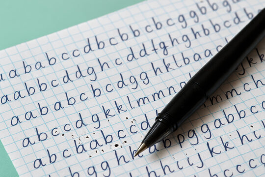Close up of pen resting on notebook with handwritten cursive alphabet practice in blue ink on squared paper