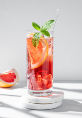 Refreshing cocktail with grapefruit, mint and ice in a glass on a marble stand on a light background