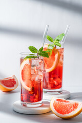 Two glasses of cocktail with grapefruit, mint and ice on marble stand on a light background