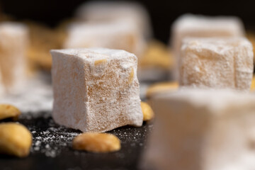 Turkish delight on the table, sugar cubes with starch and toasted peanuts on a black surface, closeup