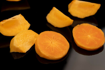 peeled ripe juicy persimmons persimmons are reflected on the black mirror surface