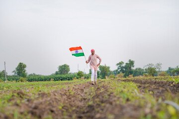 yong indian farmer holding indian flag standing at field