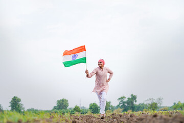 yong indian farmer holding indian flag standing at field