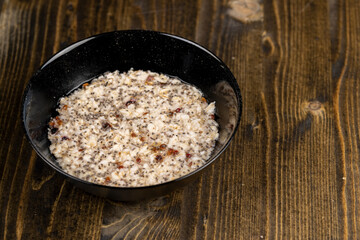 boiled oatmeal porridge with dried berries and fruits in a black bowl , cooking instant oatmeal...