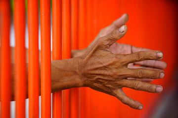 Hands Reaching Through Bright Orange Bars Symbolizing Imprisonment