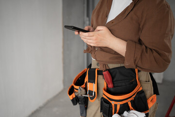 female builder with smartphone and working tools on belt, close-up. repair, renovation,...