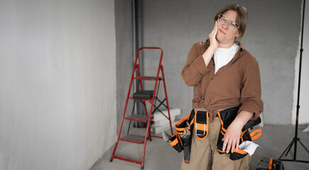 Repairwoman with tool belt in living room interior doing a home renovation, suffering teeth pain....