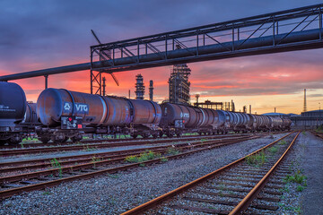 Marshalling yard at sunset with liquid transport train wagons and petrochemical industry on the background, Port of Antwerp, Belgium 