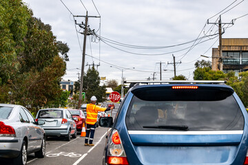 Obraz na płótnie Canvas Traffic controller directing vehicles with a stop sign during roadwork on a suburban Australian street. Cars are queued as part of temporary traffic management near a construction zone in Melbourne.