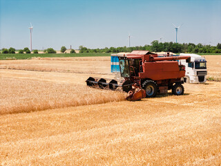 Harvest season combine harvester in golden field with sustainable energy turbines