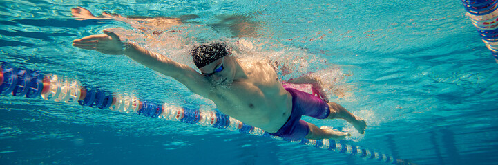 A male swimmer performs a freestyle stroke in a clear blue swimming pool. Concept of athleticism,...