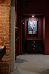 Abstract painting featuring geometric face hanging on dark wall above black cabinet with books,...