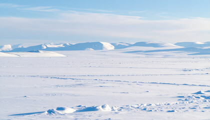 Obraz premium the image depicts a vast, snow covered landscape under a light blue sky with faint cloud formations. in the distance, there are rolling hills or small mountains entirely blanketed in snow