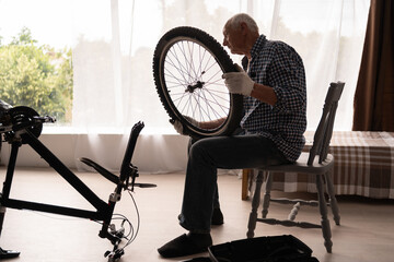Active senior man adjusting bicycle wheel at home. Bike repair, diy maintenance. cycling hobby