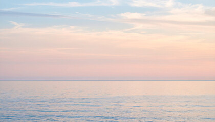 Fototapeta premium the photo showcases a serene scene of still water meeting a pastel colored sky. the water's surface is calm, reflecting the colors above with a soft, shimmering quality
