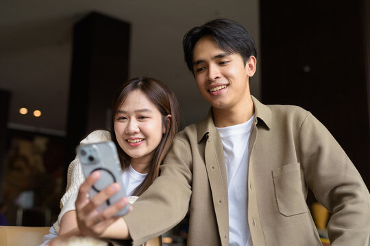 portrait of a happy young couple taking selfie in cafe with mobile phone