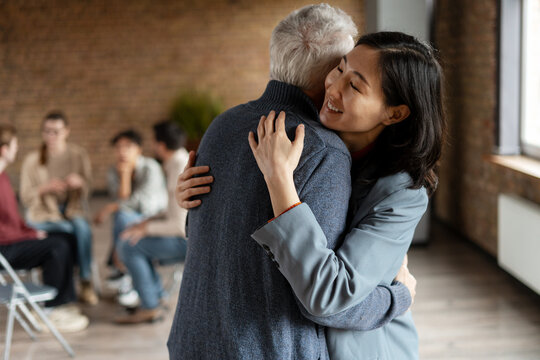 Asian business coach hugging senior patient during group therapy session